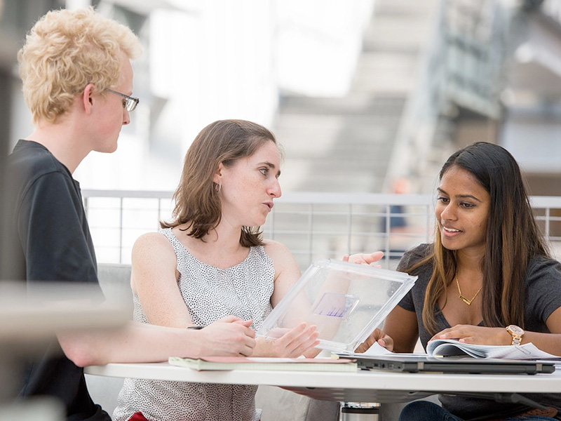 Two students meet with a professor at a table in the CBIS building