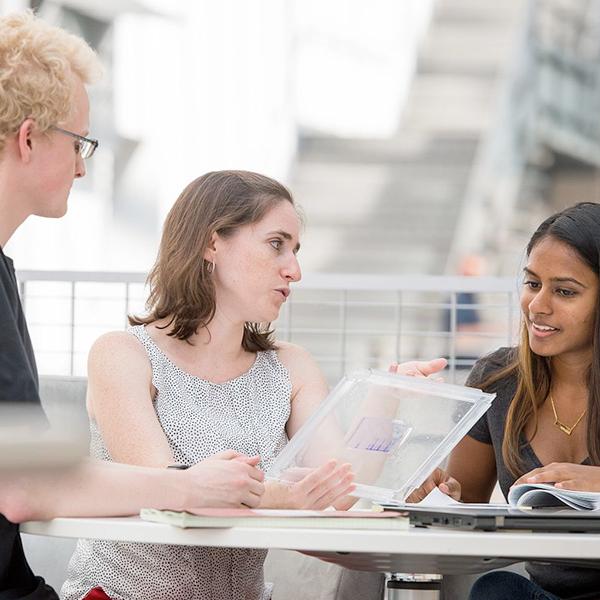 Two students meet with a professor at a table in the CBIS building